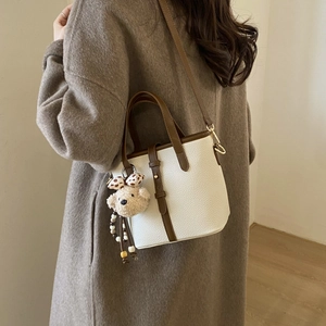 Detail of minimalist bucket bag with brown straps and plush bear charm on camel coat