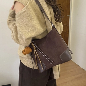 Detail view of dark brown suede bucket bag with plush bear charm and woven rope accent
