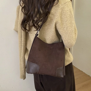 Detail of dark brown suede bucket bag with leather reinforced corners on model