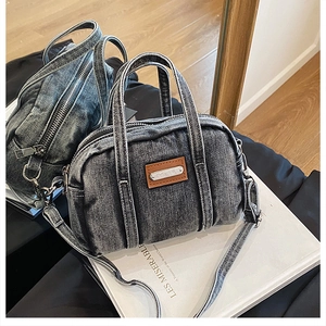 Detail of grey washed denim Boston bag with brown leather label and metal zipper closure