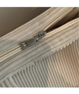 Detailed close-up of smooth silver metal zipper on cream corduroy tote bag surface