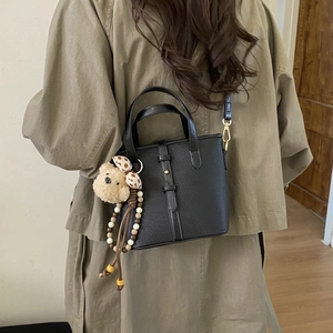 Close-up of black lychee grain leather bucket bag with cute brown bear plush charm