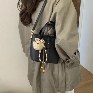 Detail of black pebbled leather bucket bag with cute bear charm and colorful beads