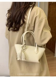 Close-up of minimalist cream-white bucket bag with double tassels on a stylish trench coat