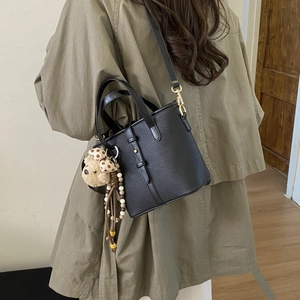 Detail of black pebbled leather bucket bag with cute bear charm and gold metal buckle