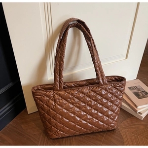 Detail of a brown quilted puffer tote bag featuring a diamond pattern on a wooden floor