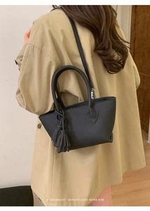 Detail of black pebbled leather bucket bag with tassel charm and long shoulder strap
