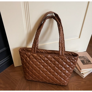 Brown quilted tote bag with diamond pattern on wooden floor in warm indoor setting