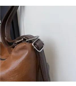 Detail of adjustable leather strap and dark metal buckle on brown shoulder bag
