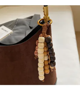 Detail of multi-color wooden bead keychain with braided rope on brown suede tote bag