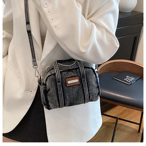 Detail of dark gray denim crossbody bag featuring brown leather patch and metal trim