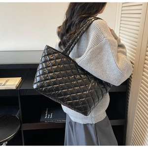 Close-up of black quilted puffer tote bag in glossy material worn by a model