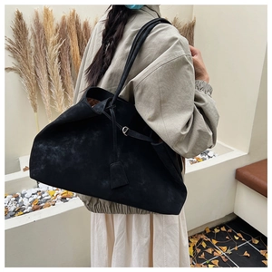 Macro detail of black suede tote bag featuring slim shoulder straps and silver buckle accents
