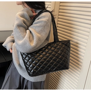 Side view of a large black quilted tote bag worn by a model in a casual setting