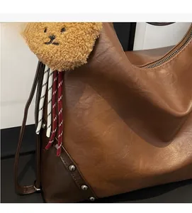 Detail of brown leather tote bag featuring a plush bear charm and metallic rivets