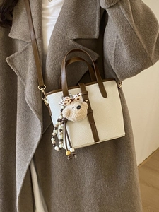 Chic cream pebble leather bucket bag with brown handles and plush bear charm on coat