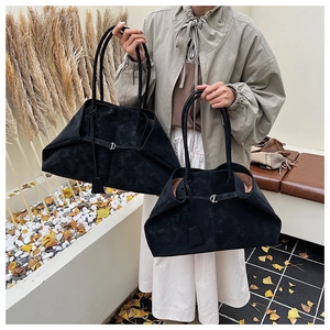 Detail of large black suede tote bag with slim straps and metal buckle in autumn setting