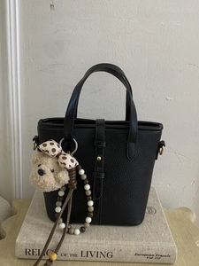 Chic black litchi pattern bucket bag with cute bear charm on vintage book background
