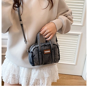 Detail of gray washed denim crossbody bag with top handles and adjustable strap