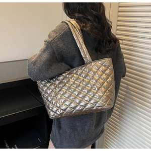 Close-up of silver quilted tote bag with metallic finish shown on model in modern setting