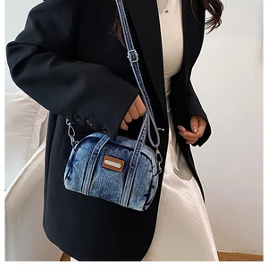 Detail of blue washed denim mini crossbody bag featuring leather tag and silver pendant