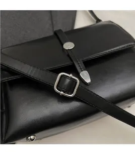Détail de la bandoulière réglable à boucle argentée sur un sac à rabat en cuir noir