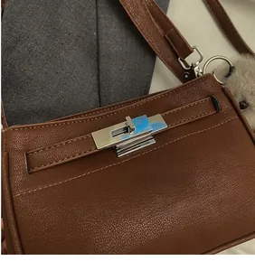 Detail of brown litchi pattern bag with silver turn-lock and grey faux fur charm