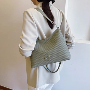 Dettaglio della borsa a pieghe verde chiaro con trama a nido d'ape su un completo beige
