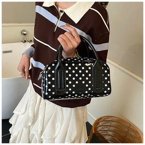 Polished black leather Boston bag with white polka dots held by model in soft indoor setting