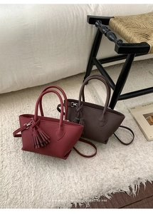 Detailed close-up of textured leather bucket bags in burgundy and dark brown with tassels