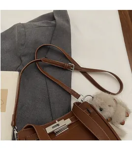 Detail of brown faux leather crossbody bag with silver twist lock and capybara plush charm