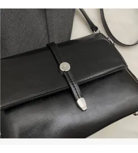 Gros plan du sac bandoulière en cuir noir avec boucle ronde argentée et texture raffinée