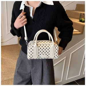 Close-up of white polka dot leather handbag with branded logo and top handle detail