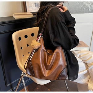 Brown vintage faux leather tote with metal rivets and cute bear charm shown on a chair