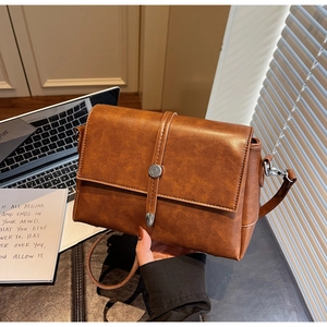 Detail of vintage brown crossbody bag featuring silver round buckle and textured leather