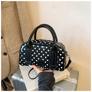 Close-up of a glossy black polka dot Boston bag featuring double handles and metal hooks