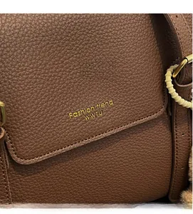 Gros plan sur un sac cabas en cuir grainé marron avec logo doré et perles