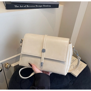 Detail of cream flap shoulder bag with silver cylindrical buckle and matte leather texture