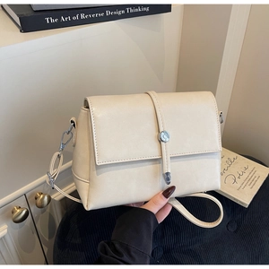 Close-up of cream square flap bag featuring a retro round metal twist lock and matte finish