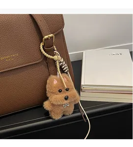 Détail d'un porte-clés chien en peluche marron avec plaque en métal sur un sac en cuir