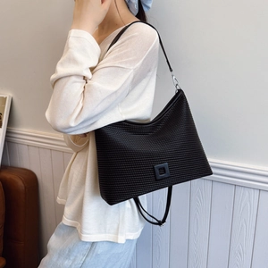 Dettaglio della borsa tote nera plissettata con trama intrecciata e placca decorativa a rilievo