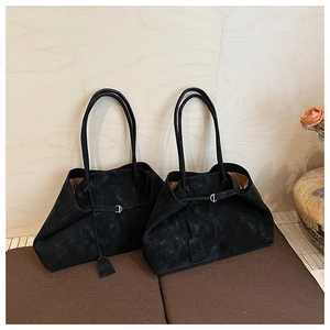 Detail of minimalist black matte leather tote bag with slender straps and metal buckle