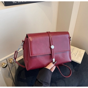 Detail of burgundy vintage crossbody bag with a silver cylinder lock and leather strap