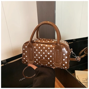 Detail of a brown Boston bag with white polka dots and an adjustable shoulder strap