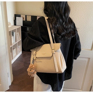 Détail du sac cabas en cuir grainé beige avec un pendentif ours en peluche et boucles dorées