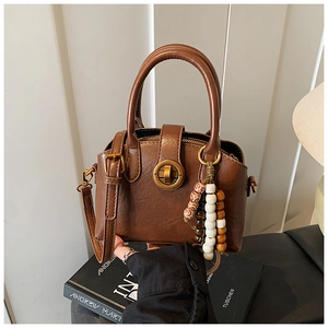 Detail einer braunen Vintage-Muscheltasche mit Holzperlen-Anhänger und Metall-Drehverschluss