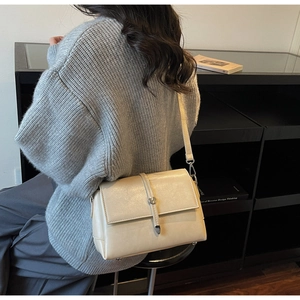 Detail view of a cream shoulder bag with vertical leather strap and metal buckle