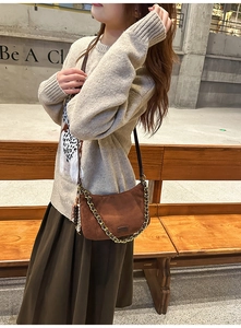 Detail of brown faux suede shoulder bag with gold chain and vintage charm