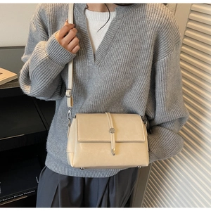 Détail du sac bandoulière crème avec fermoir rotatif argenté et pieds en métal au fond