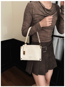 Detail of cream-colored square handbag featuring golden hardware and logo with leather texture